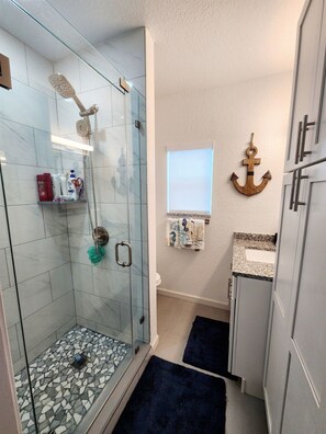 Ein modernes Badezimmer mit einer gläsernen Duschkabine, einem Waschtisch mit Granitplatte und einem dekorativen Anker an der Wand.