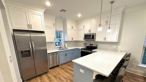 A modern kitchen with white cabinets, stainless steel appliances, and a wooden floor. - Hollywood House - Luxurious New Build With 6 Seat Golf Cart! (Bay St. Louis)