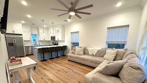 A modern kitchen with white cabinets, a central island with bar stools, a built-in oven, and a ceiling fan. - Hollywood House - Luxurious New Build With 6 Seat Golf Cart! (Bay St. Louis)
