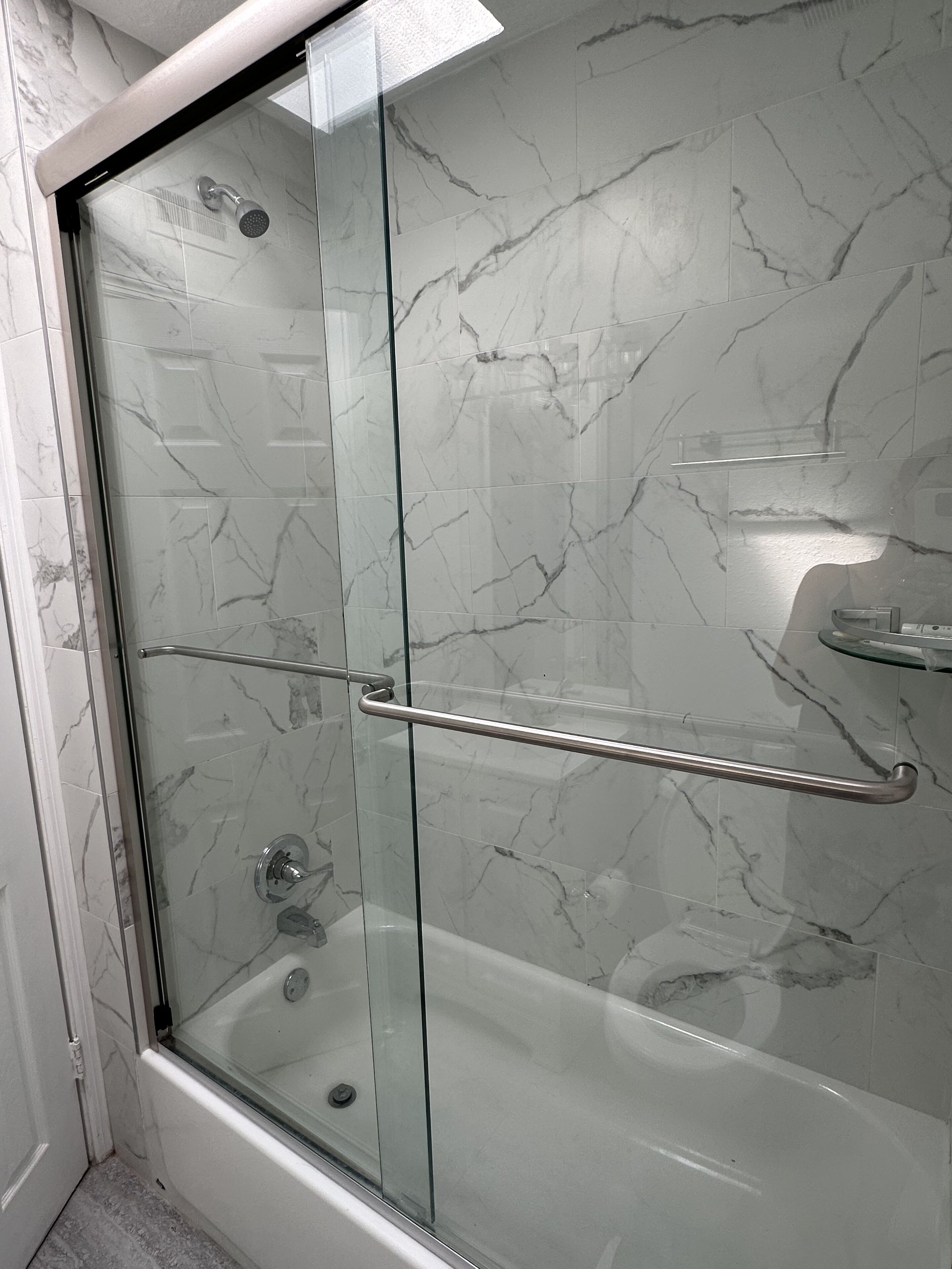 Een douche met glazen wanden, een betegelde muur van marmer en een metalen handgreep.