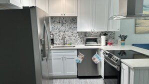 A modern kitchen with white cabinets, a stainless steel refrigerator, a toaster, and a dishwasher. - Beach Block Apartment w/ Balcony (Clearwater)