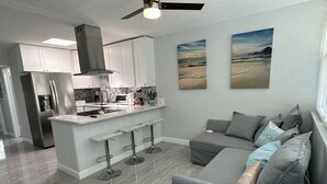A modern kitchen with a central island, bar stools, and a grey sofa with cushions. - Beach Block Apartment w/ Balcony (Clearwater)