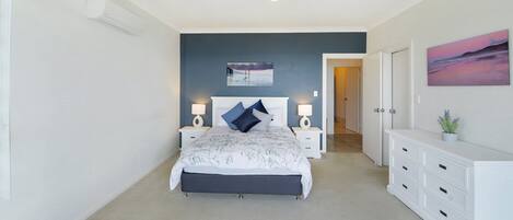 A bedroom with a bed, bedside tables, a dresser, a painting, and a hallway.