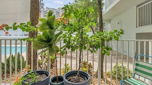 A balcony with potted plants, a bench, and a view of a swimming pool and buildings. - Key Biscayne Gem — Steps to Beach, Pool Views, King Bed, Parking (Key Biscayne)