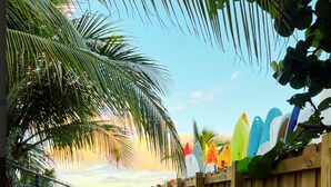 A wooden fence with surfboards on top, a brick pathway, and a palm tree. - Key Biscayne Gem — Steps to Beach, Pool Views, King Bed, Parking (Key Biscayne)