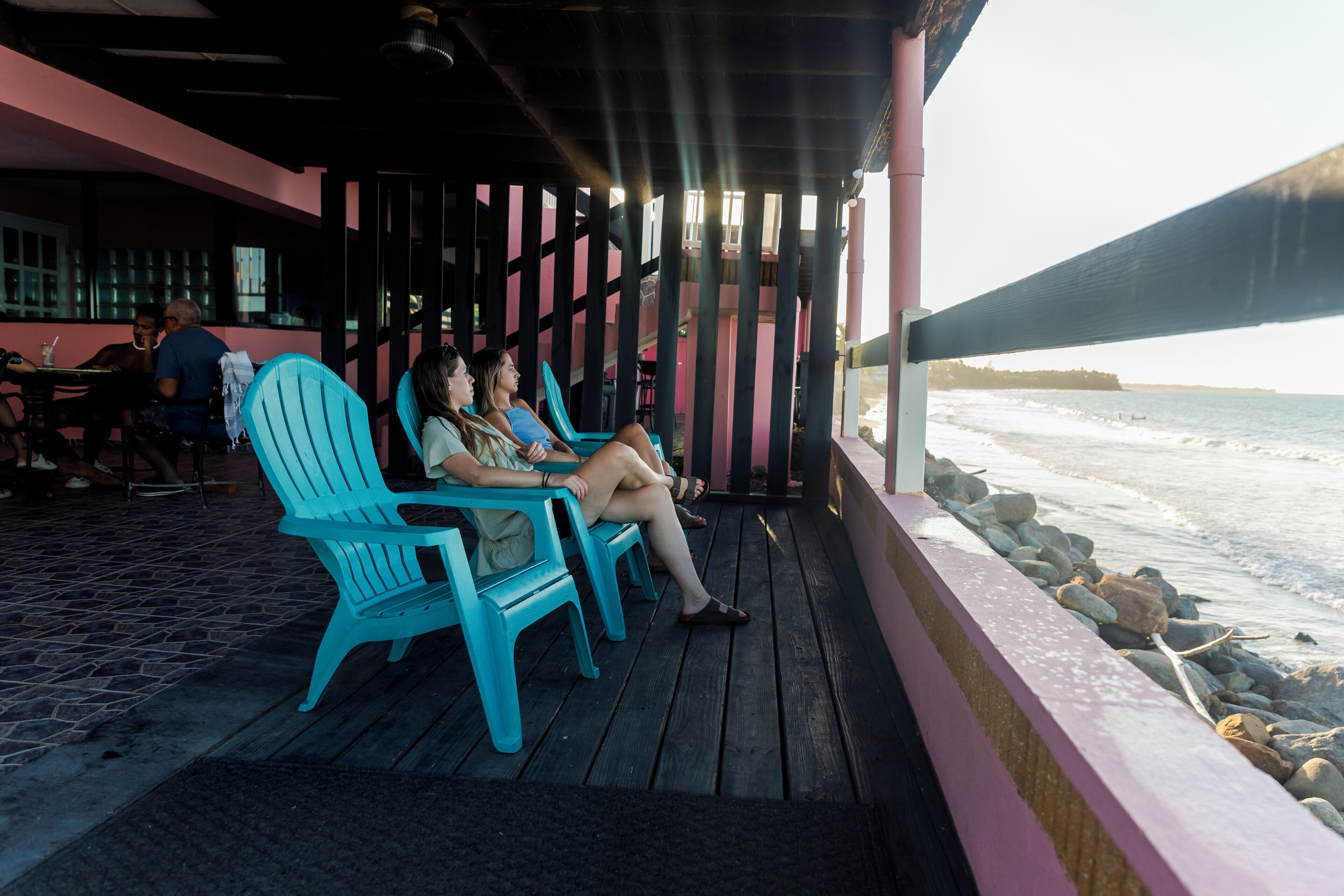 A covered outdoor seating area with chairs, a wooden deck, and a view of the ocean.