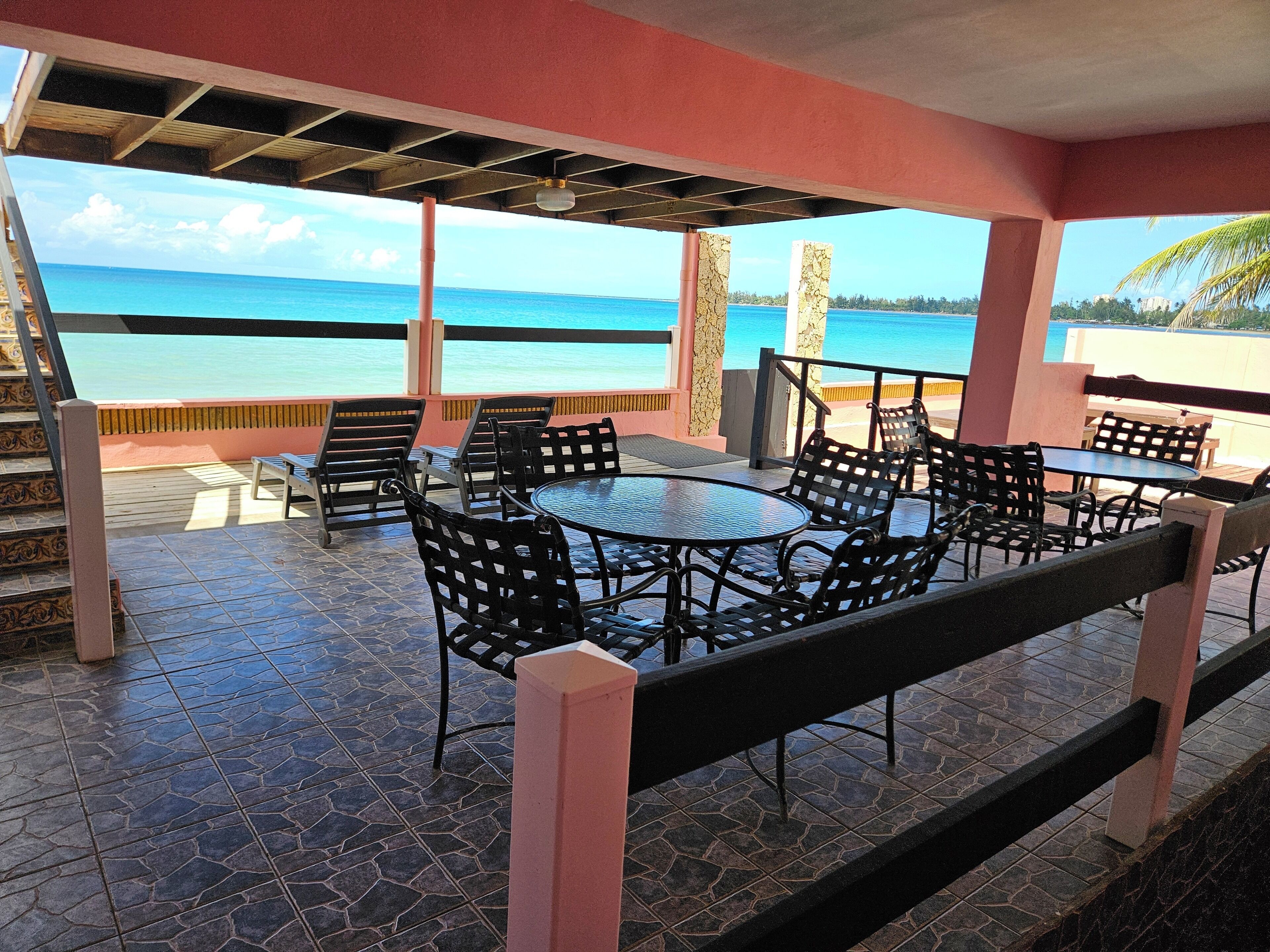 Une terrasse extérieure offrant une vue sur l’océan, avec une table ronde et plusieurs chaises.
