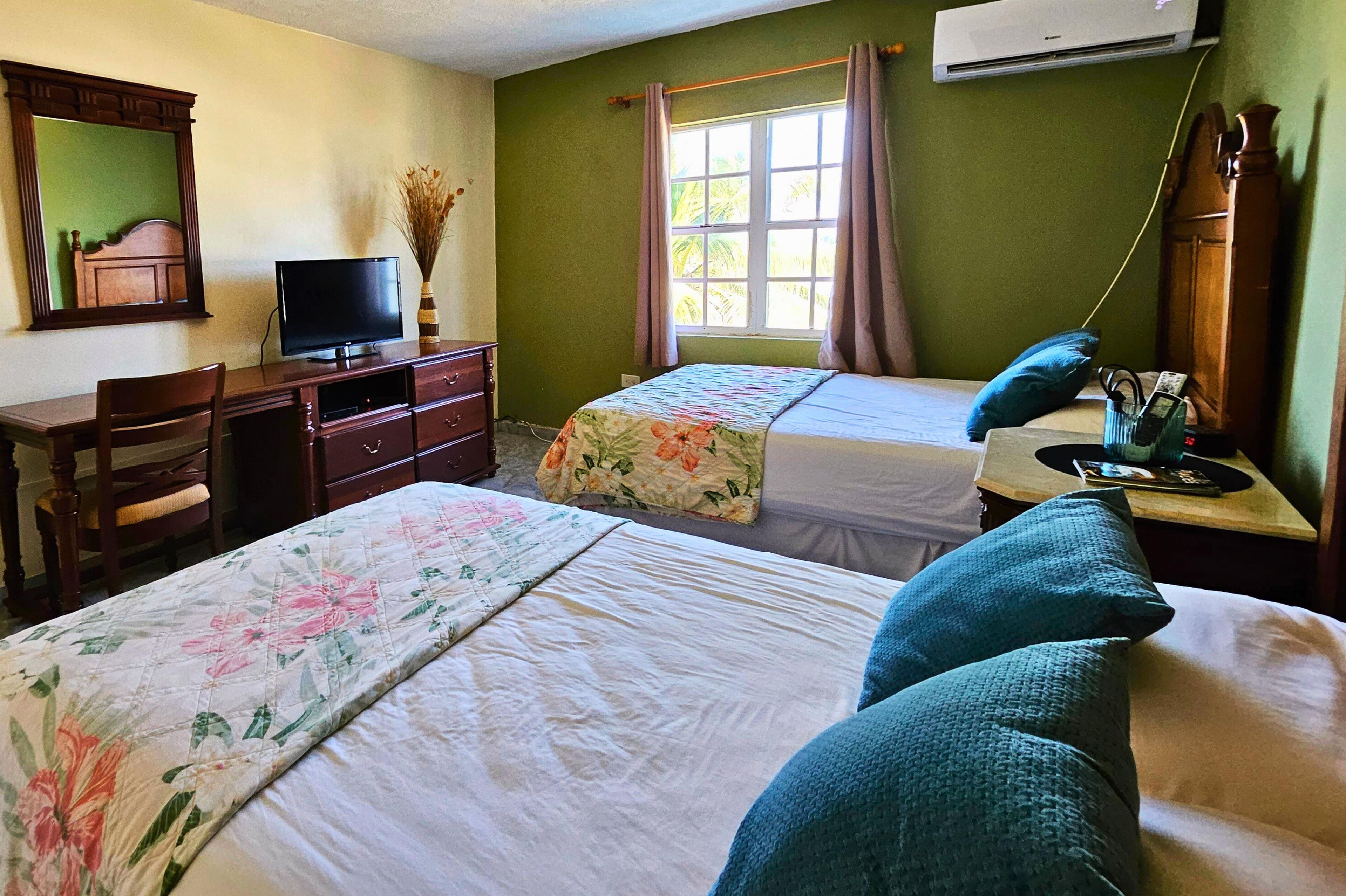 Una habitación de hotel con dos camas, un escritorio con televisor, un aparador y un equipo de aire acondicionado.