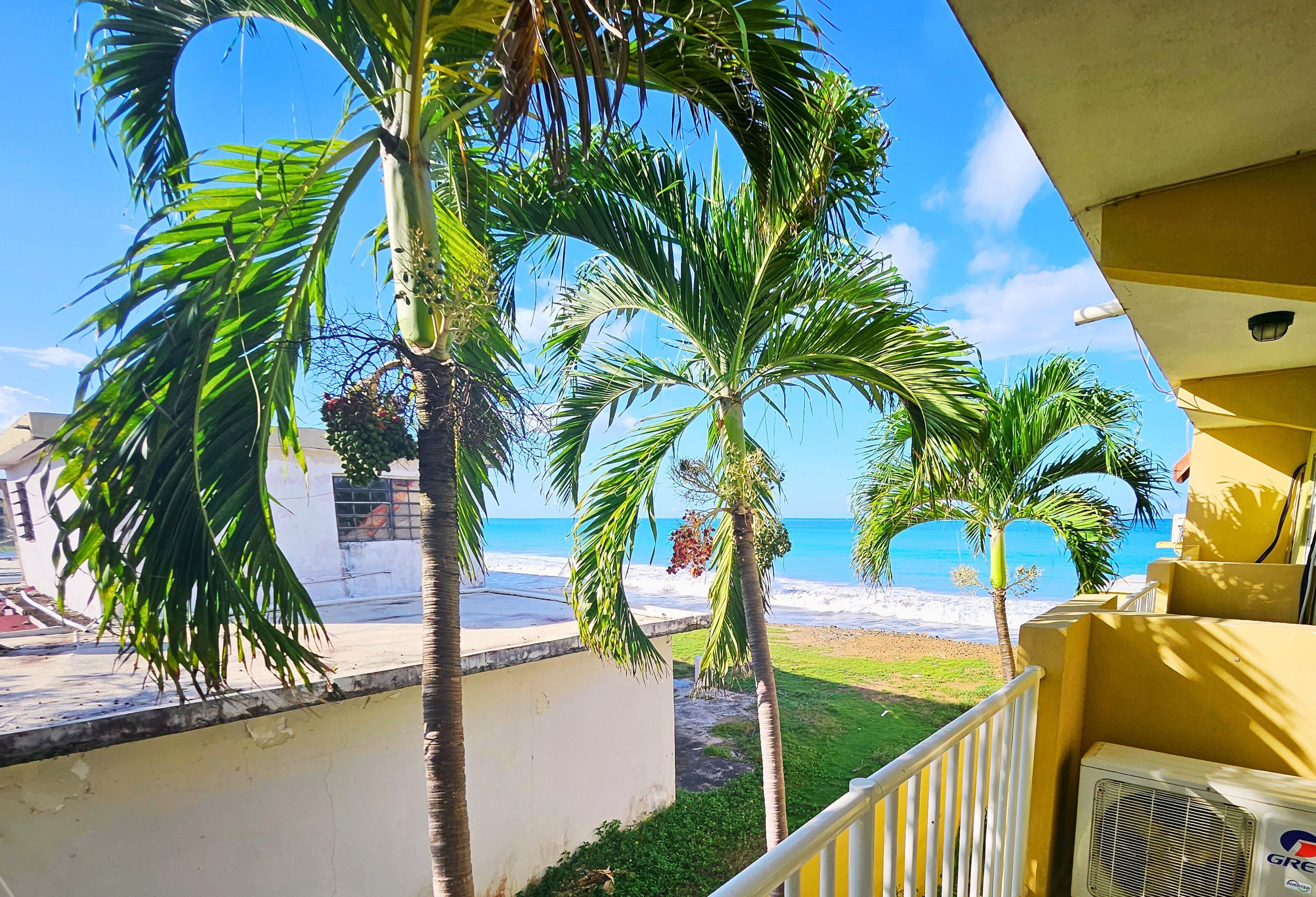 A balcony with a view of the beach, palm trees, and a clear sky.