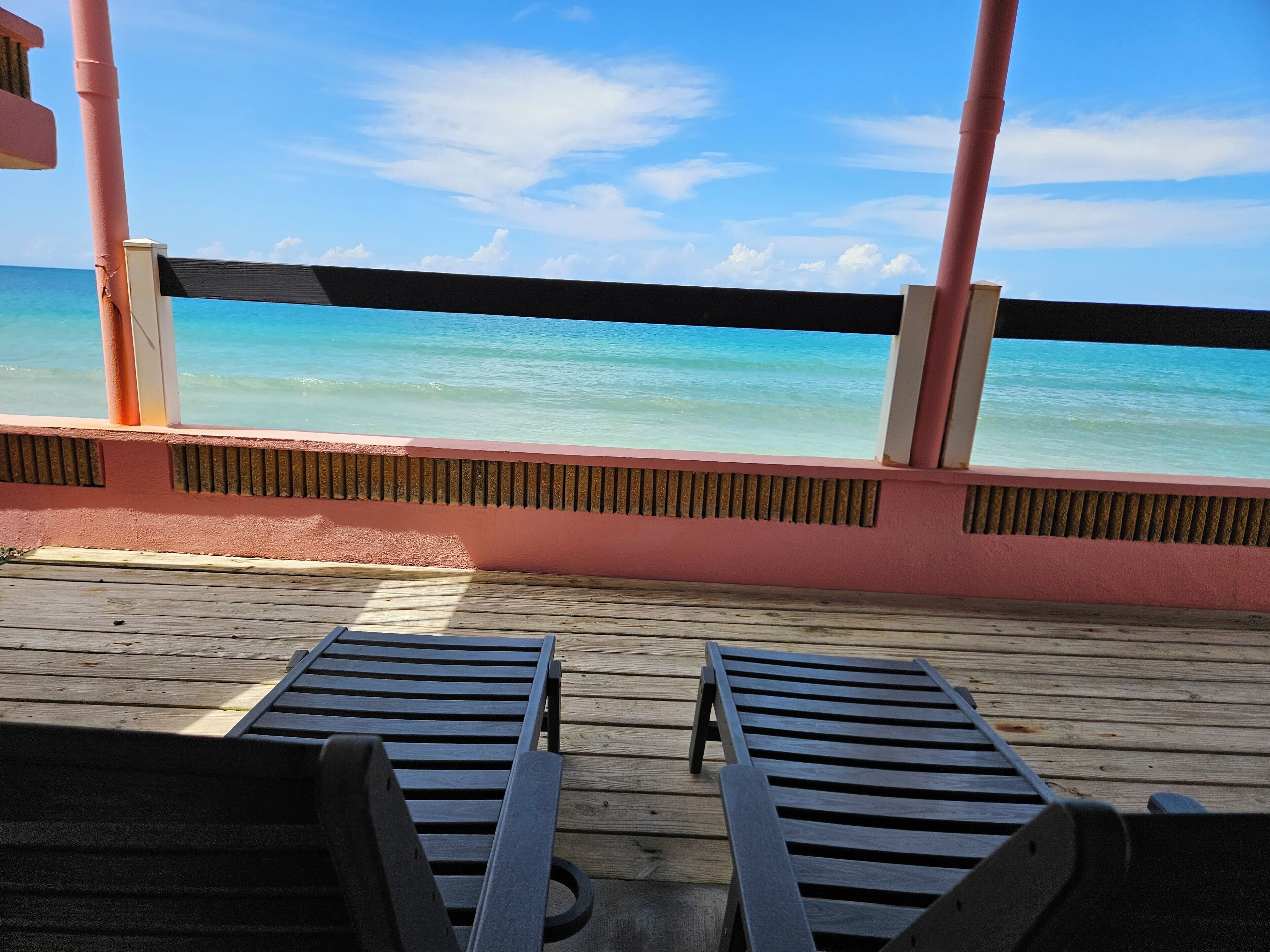 A wooden deck with two lounge chairs facing a beach.