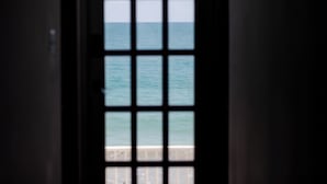 Blick durch ein Fenster mit Gittermuster auf ein Gewässer.