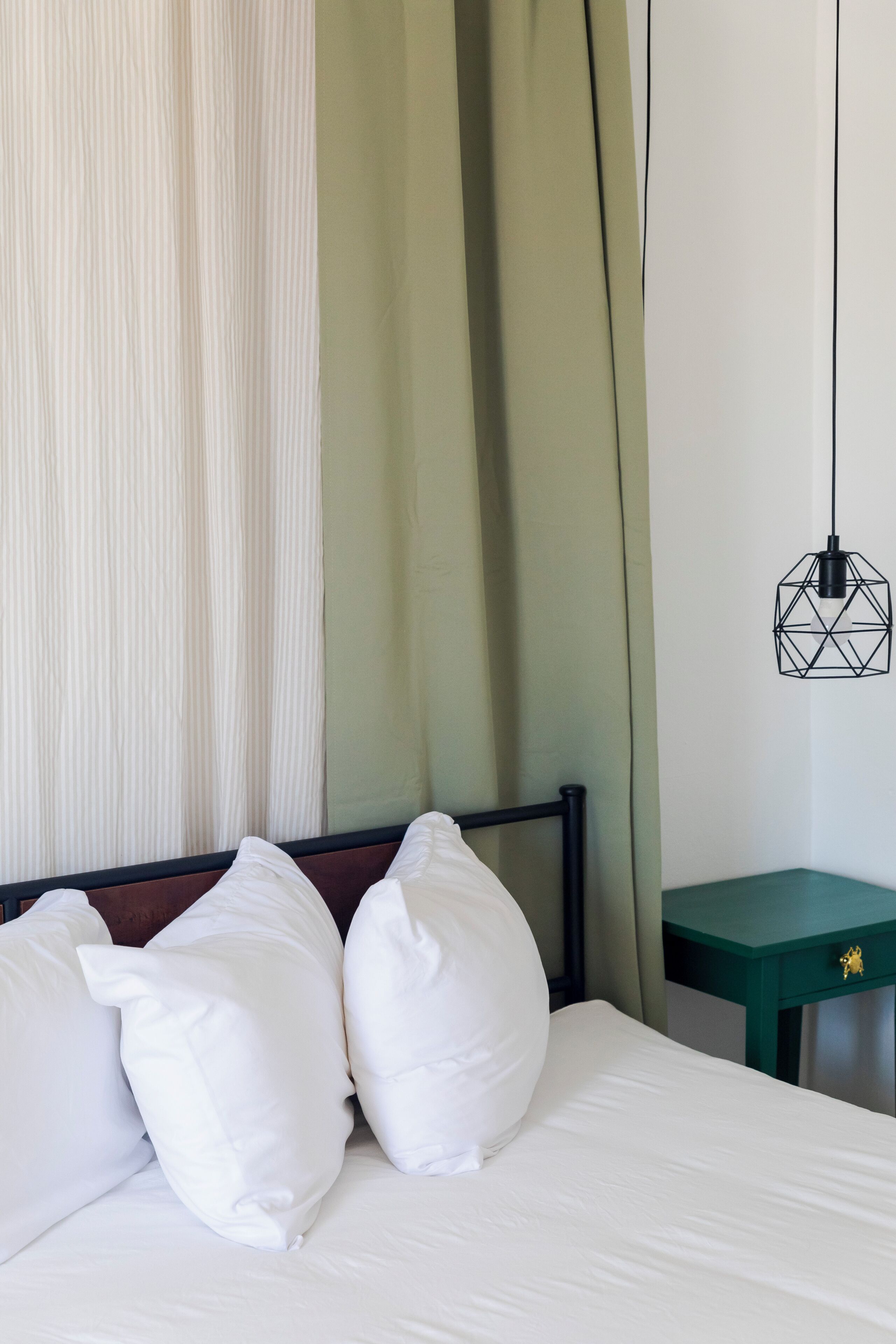 A bed with white pillows, a green nightstand, and a geometric pendant light.