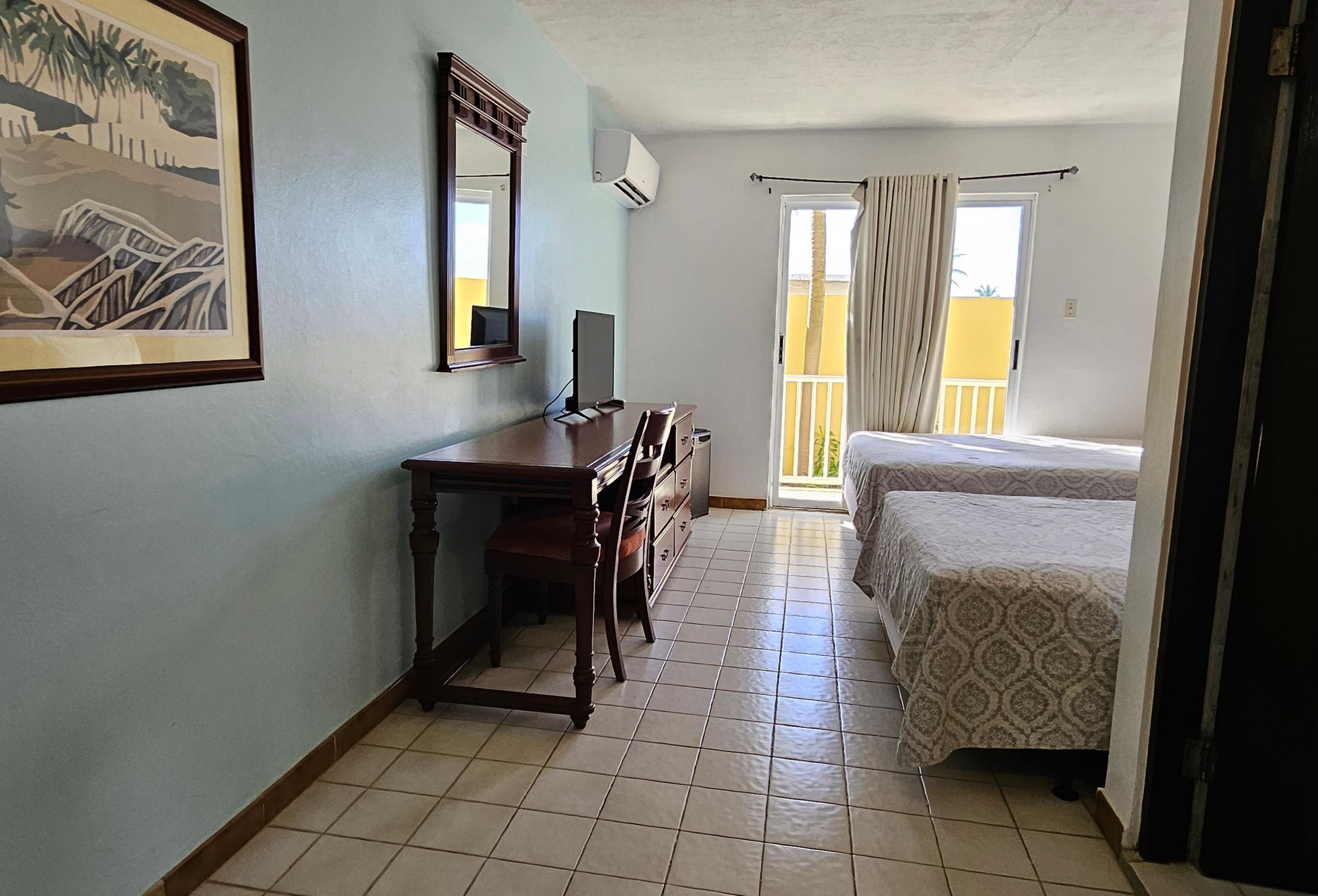 A hotel room with a desk, a chair, a bed, a window with curtains, and a balcony.