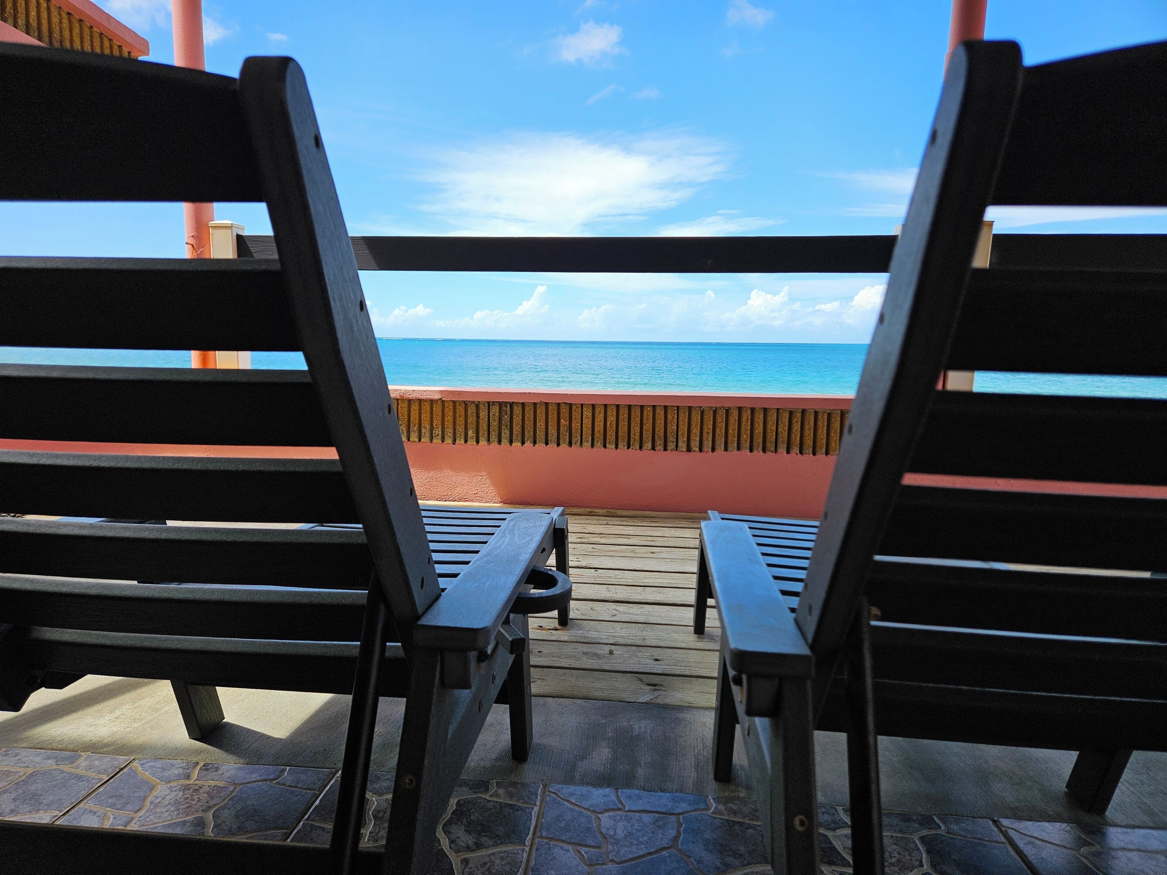 Two wooden lounge chairs facing a wooden deck with a view of the ocean.
