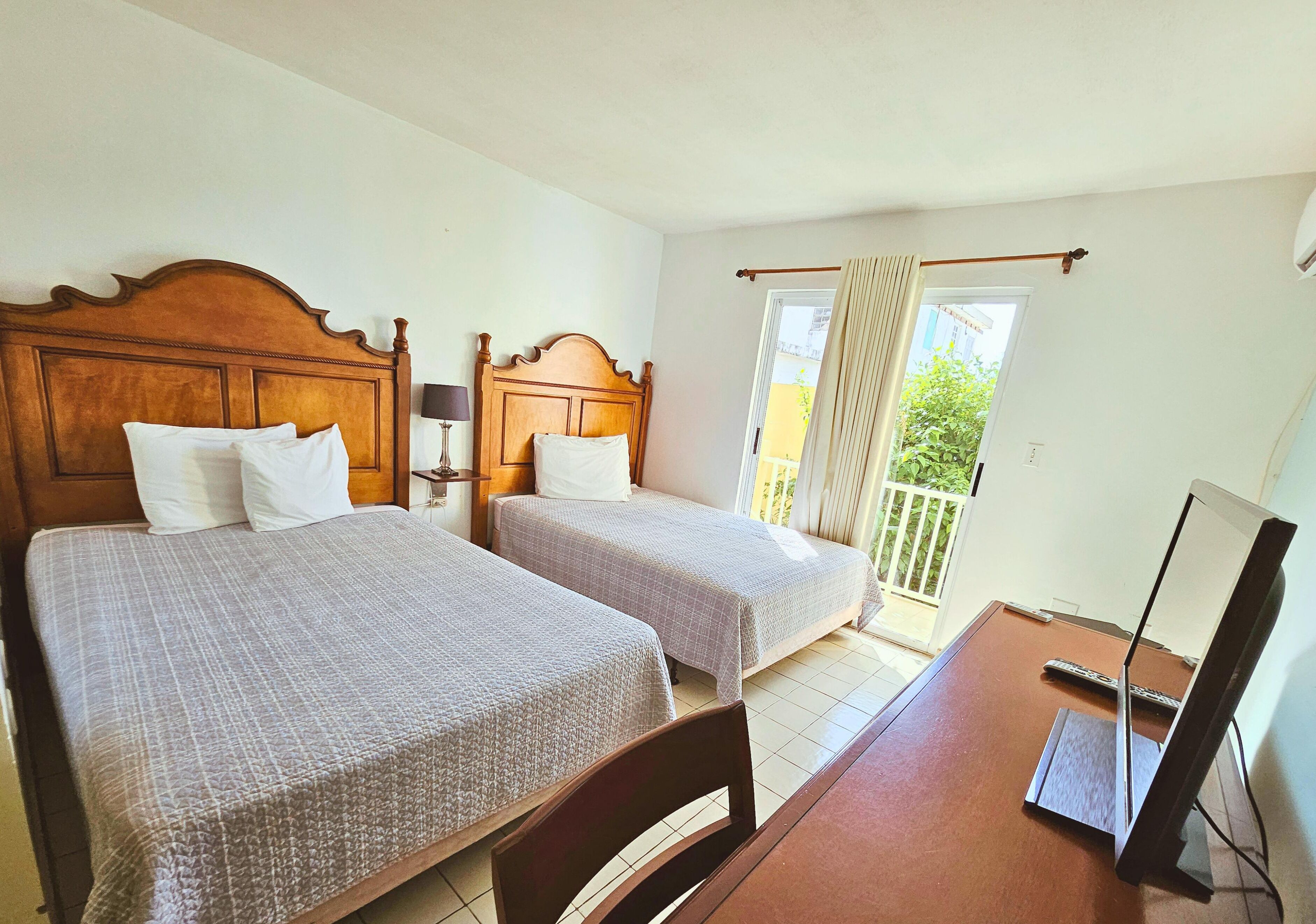 Habitación de hotel con dos camas, un escritorio con ordenador y vistas al exterior.