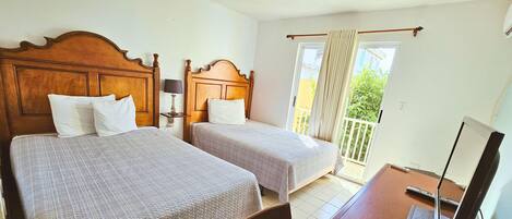 Habitación de hotel con dos camas, un escritorio con ordenador y vistas al exterior.