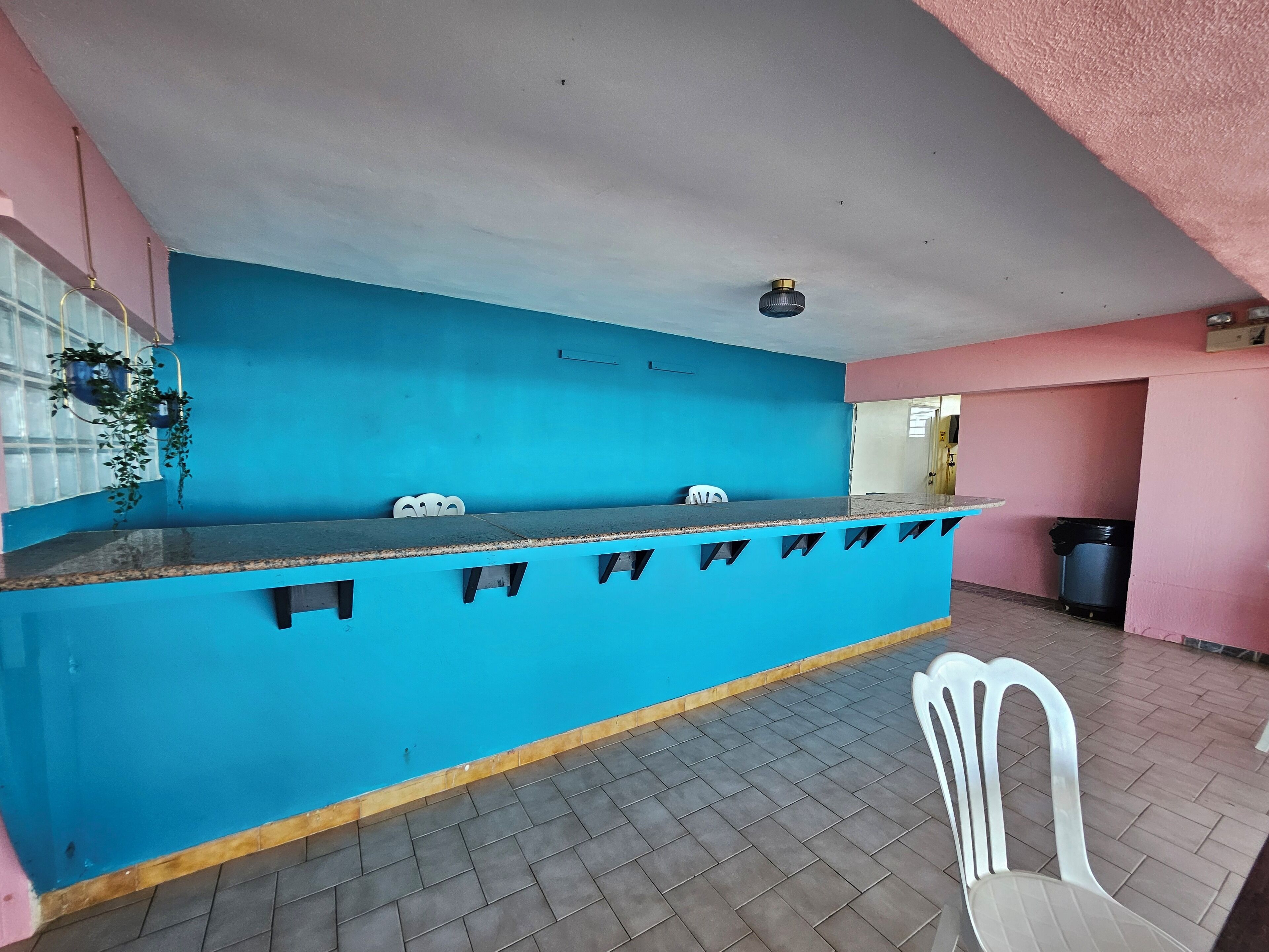 A blue counter with a white chair, a trash bin, and a ceiling fan.