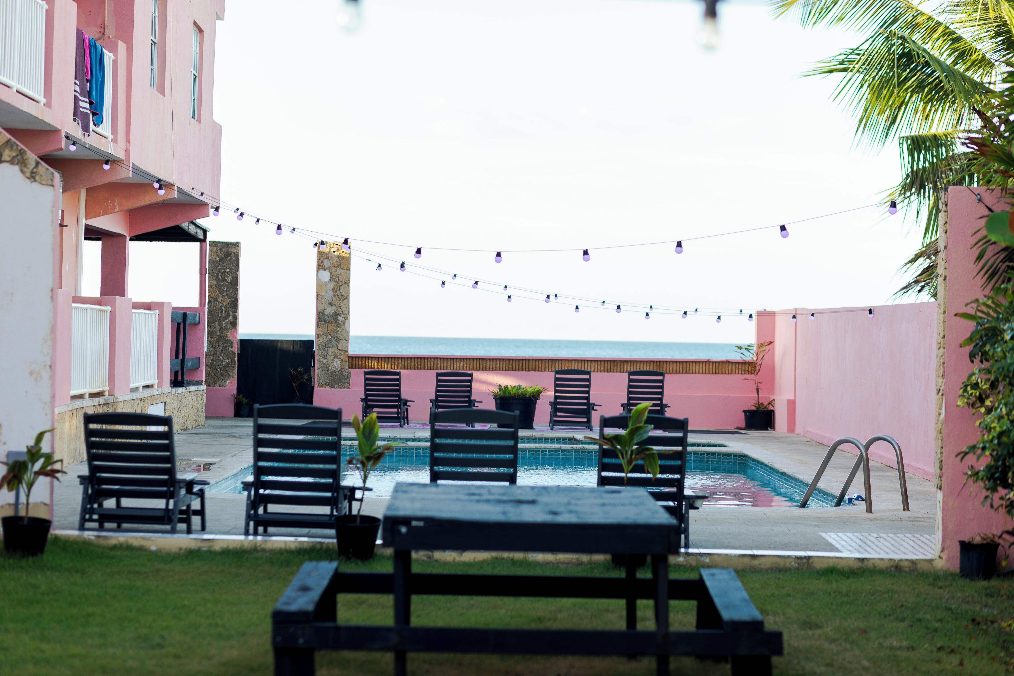 An outdoor pool area with lounge chairs, a table, and string lights.