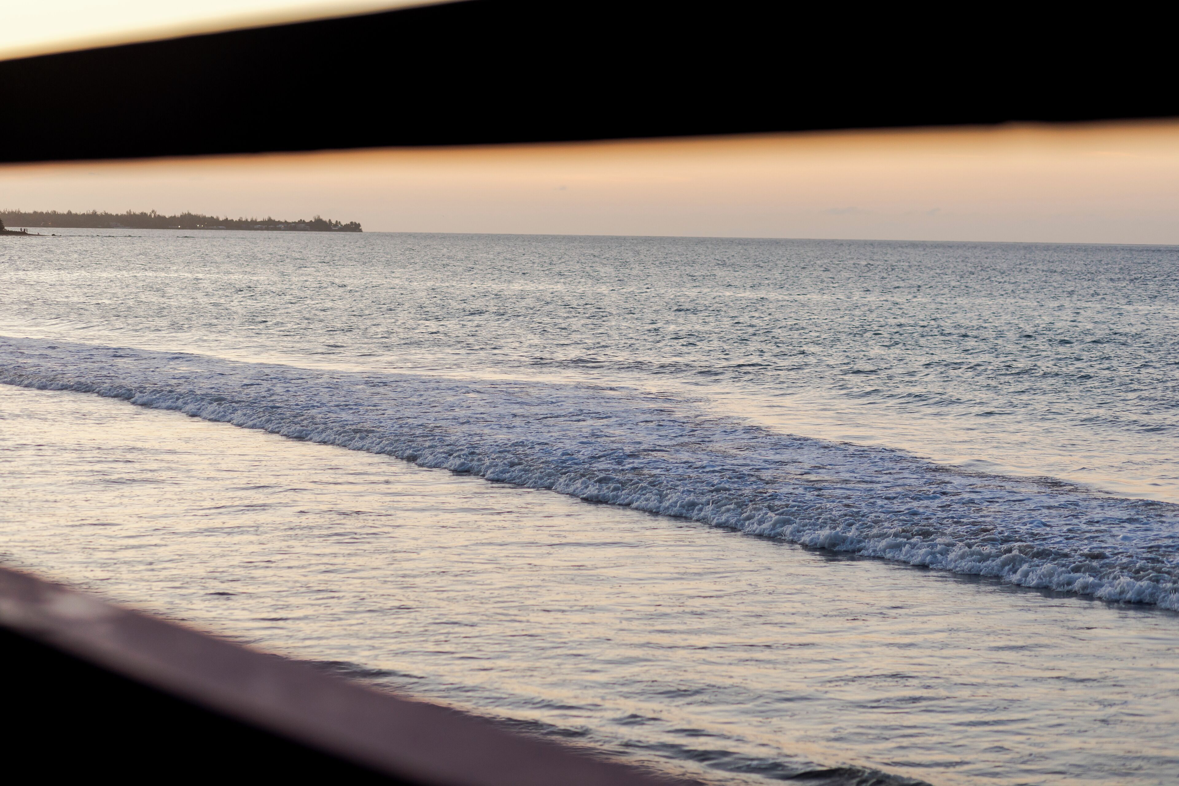A view of the ocean with waves, a distant shoreline, and a clear sky.