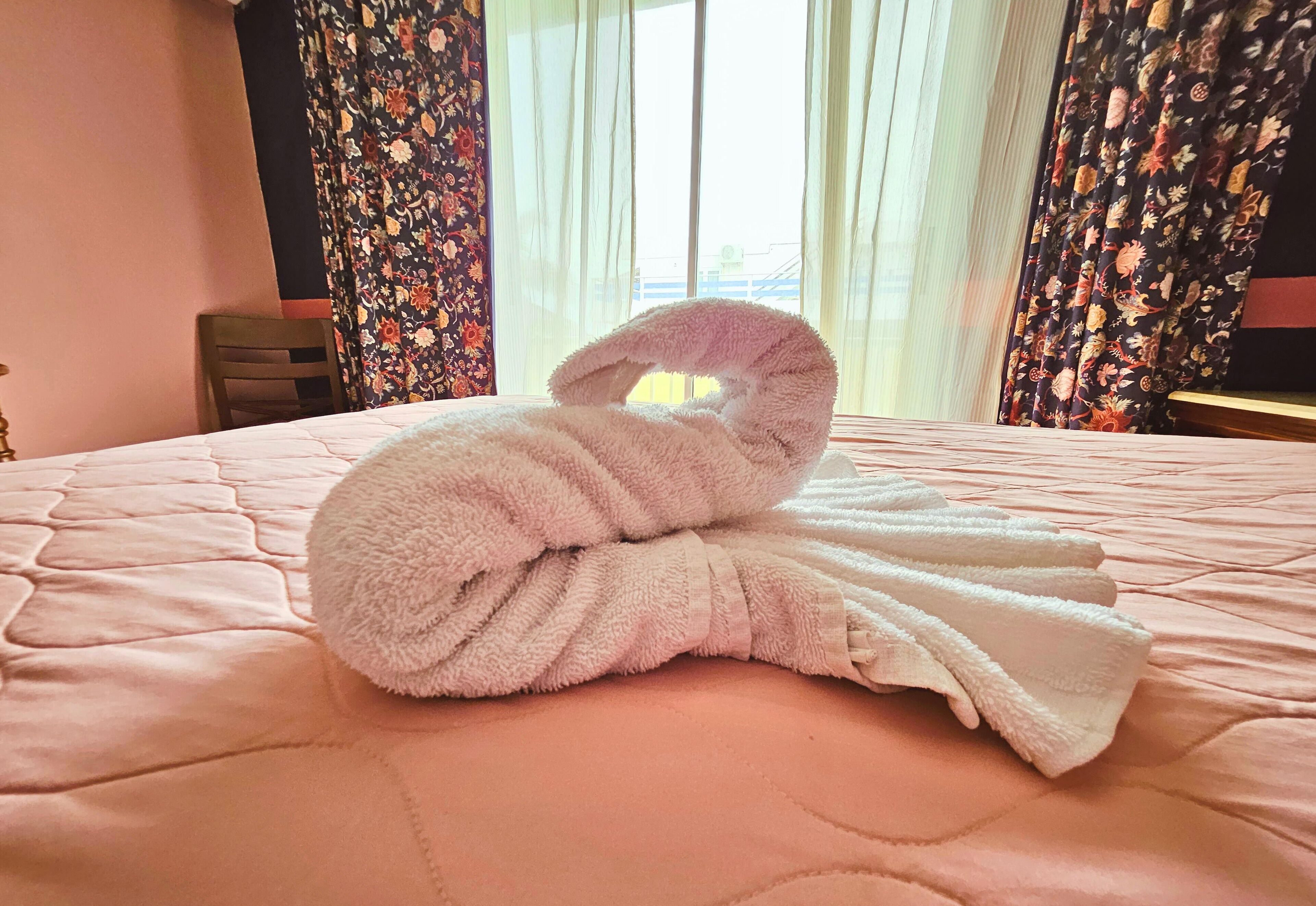 Een keurig opgemaakt bed, met een roze en witte handdoek in het midden gevouwen.