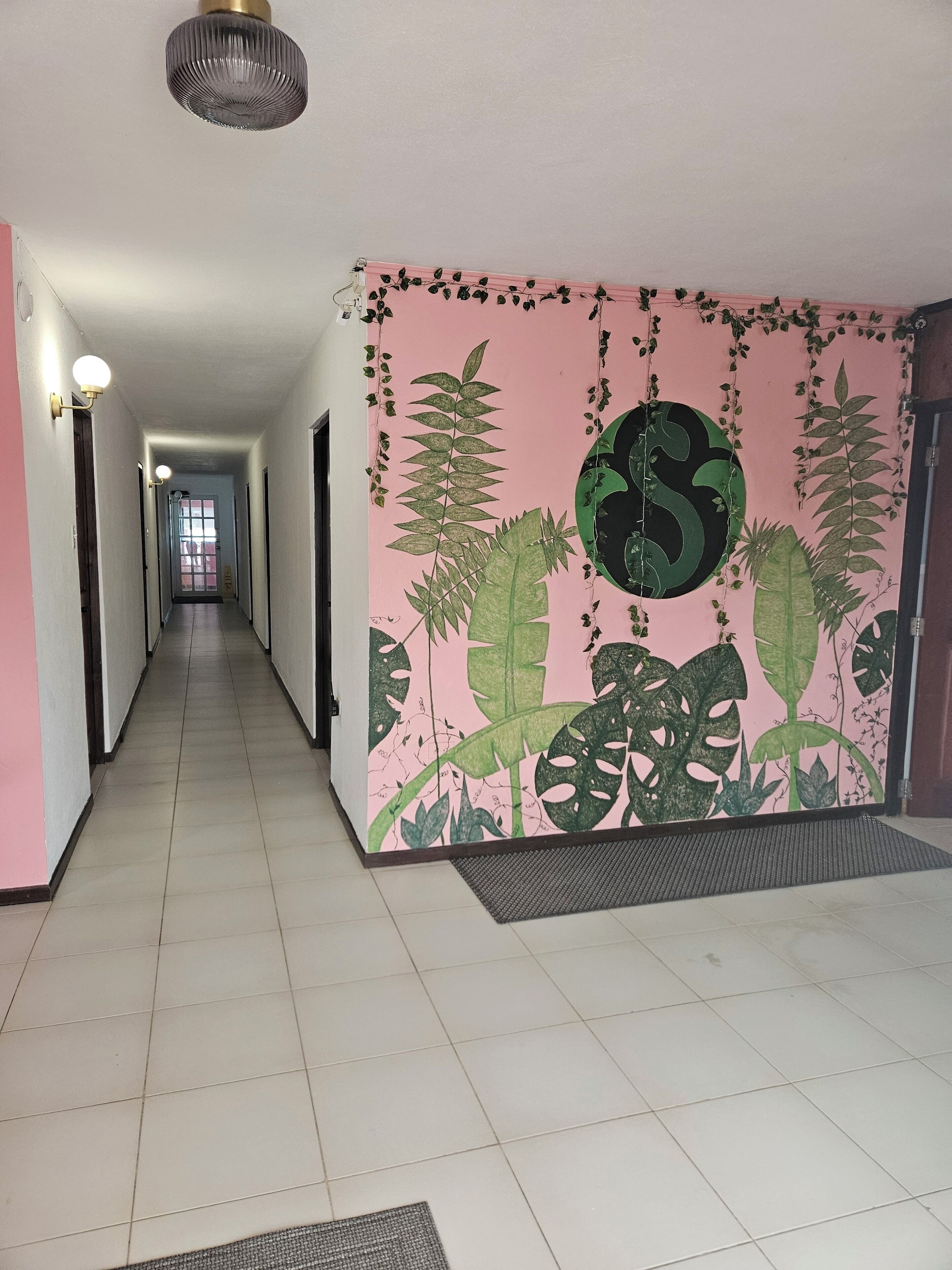 Un pasillo con pared rosa que presenta un gran diseño de hojas verdes y un motivo circular.