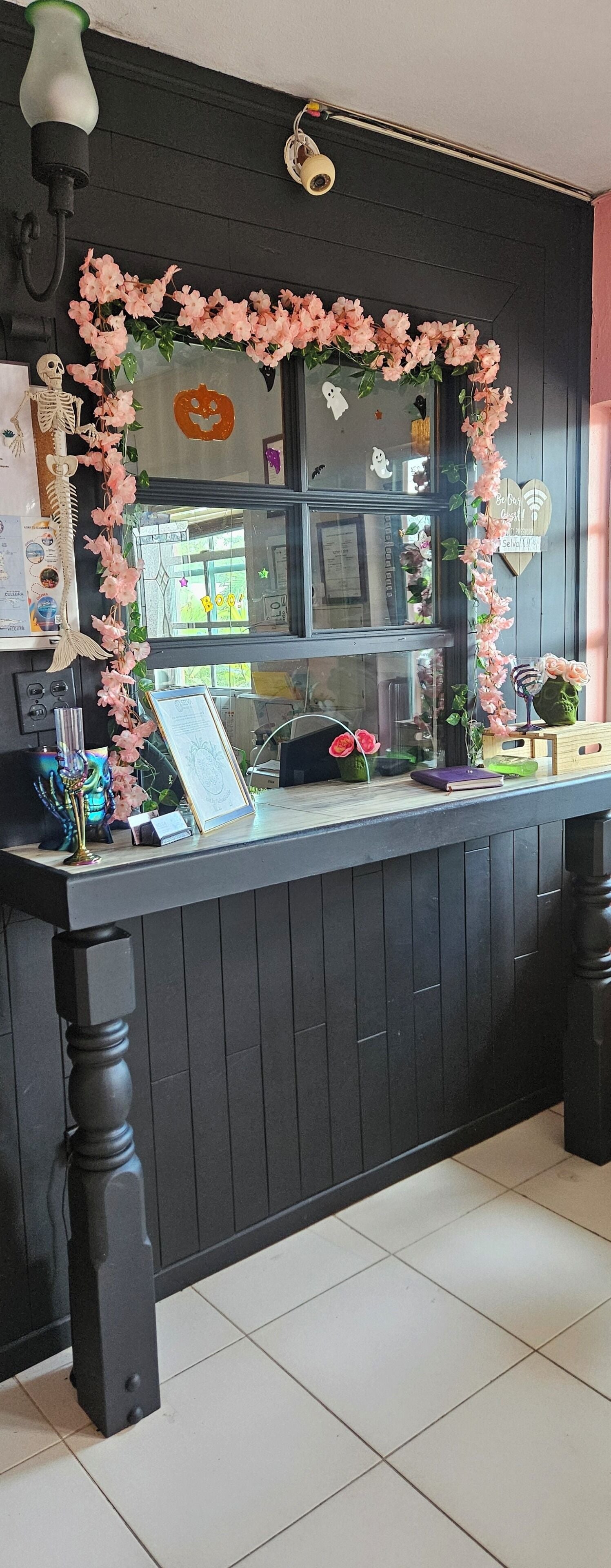 A reception desk with a mirror, framed by pink flowers, and a Halloween decoration.