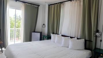 A hotel room with a large bed, a desk, a chair, a small table, and a view of greenery outside.