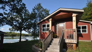 A cabin with a wooden staircase leading to a deck, situated by a lake with a boat docked nearby. - Cuyuna Lake cabin retreat. Fish, hike, bike trails, star gazing, mins to town.  (Ironton)