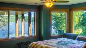 A bedroom with a bed, a chair, and a ceiling fan. There are windows with a view of trees and a lake. - Cuyuna Lake cabin retreat. Fish, hike, bike trails, star gazing, mins to town.  (Ironton)