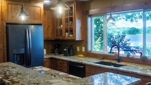 A kitchen with granite countertops, wooden cabinets, a refrigerator, and a window with a view of trees and a body of water. - Cuyuna Lake cabin retreat. Fish, hike, bike trails, star gazing, mins to town.  (Ironton)
