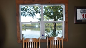 A wooden dining table with four chairs, a woven basket, and a window with a view of a lake and trees. - Cuyuna Lake cabin retreat. Fish, hike, bike trails, star gazing, mins to town.  (Ironton)