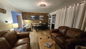 Ein Wohnzimmer mit zwei braunen Ledersofas, einem Couchtisch mit einer Zeitschrift und einem Essbereich mit Holztisch und Stühlen.