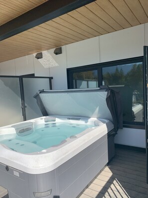 A hot tub with a wooden deck and a window overlooking a forested area.