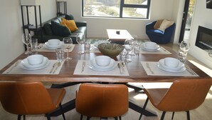 A dining area with a wooden table set for four, surrounded by orange chairs, with a view of trees and a building outside the window. - Mountain View Condo w/ Hot Tube! 2B/1B - Central between Ski Resort and Downown (Revelstoke)
