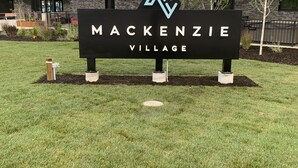 A sign for Mackenzie Village with a modern building in the background. - Mountain View Condo w/ Hot Tube! 2B/1B - Central between Ski Resort and Downown (Revelstoke)