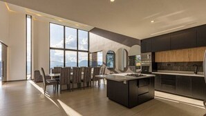 Une cuisine moderne avec des meubles de couleur sombre, un îlot central et un coin repas doté d’une grande fenêtre donnant sur un paysage montagneux.