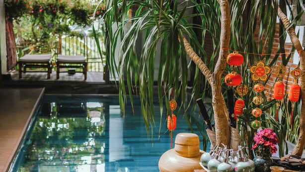 Un área de piscina con terraza de madera, una mesa con cerámica y adornos colgantes.
