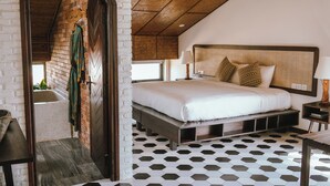 Un dormitorio con una cama grande, cabecera de madera, mesita de noche, lámpara y vista a una pared de ladrillo y una ventana.
