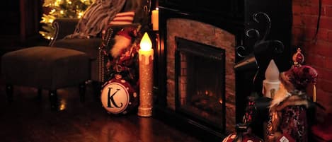 Una habitación acogedora con pared de ladrillo, un árbol de Navidad, chimenea y televisor de pantalla plana colgado encima.