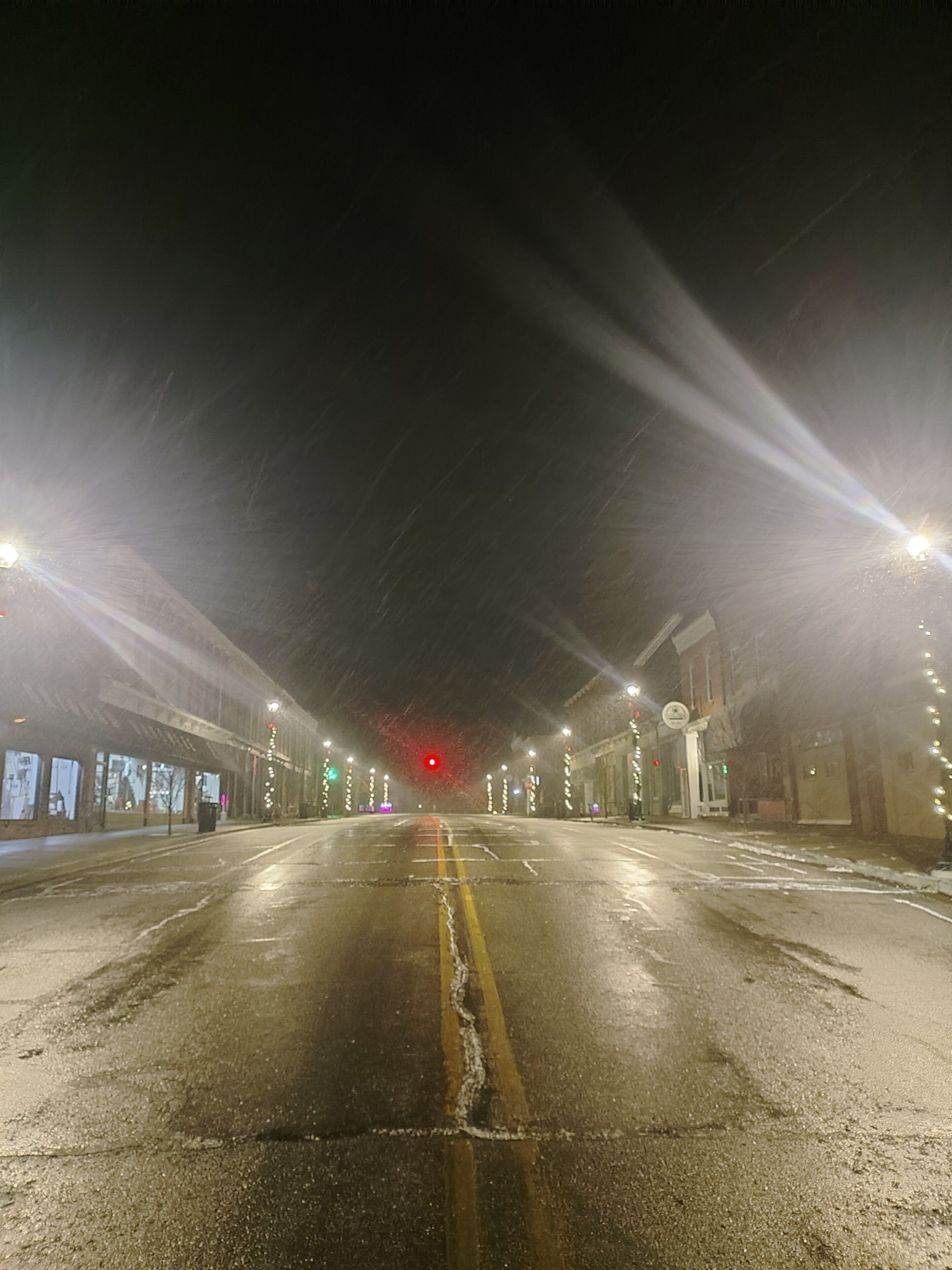 A wet road with streetlights and a red traffic light in the distance.