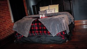 A neatly made bed with a grey blanket and plaid bedding, a bedside table with a cup and saucer, and a dark headboard. - 1800s Victorian Loft  (Concord)
