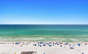 Uma praia com águas cristalinas, areal arenoso e vários guarda-sóis.