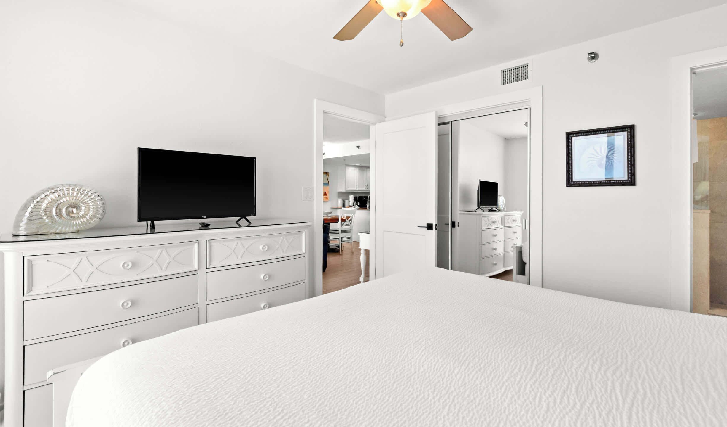 A bedroom with a bed, a dresser, a television, and a ceiling fan.