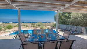 A covered outdoor area with a pool, dining table, and chairs, overlooking a scenic landscape. - Villa Kalliopi in Pernera (Paralimni)