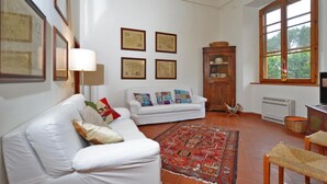 A living room with a white sofa, a red patterned rug, and a wooden cabinet. - Villa Piandisette in Cetona (Cetona)