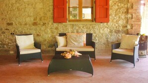 A stone-walled room with a wooden window, two wicker chairs, a sofa, and a coffee table with flowers. - Villa Piandisette in Cetona (Cetona)