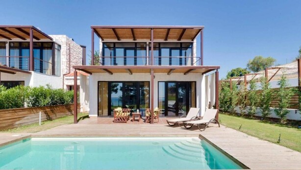 Une maison moderne à deux étages, dotée d’une piscine, d’un espace extérieur aménagé et offrant une vue sur la mer.