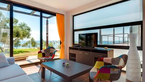 Un salon moderne doté d’un grand téléviseur, de sièges confortables et offrant une vue sur la mer.