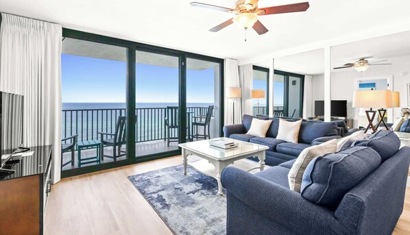 Un vaste espace de vie avec un balcon donnant sur la mer, un ventilateur de plafond et un aménagement intérieur moderne.