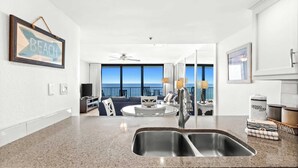 A modern kitchen with a large window, a dining area, and a view of the ocean. - One Seagrove Place 0908 (Santa Rosa Beach)